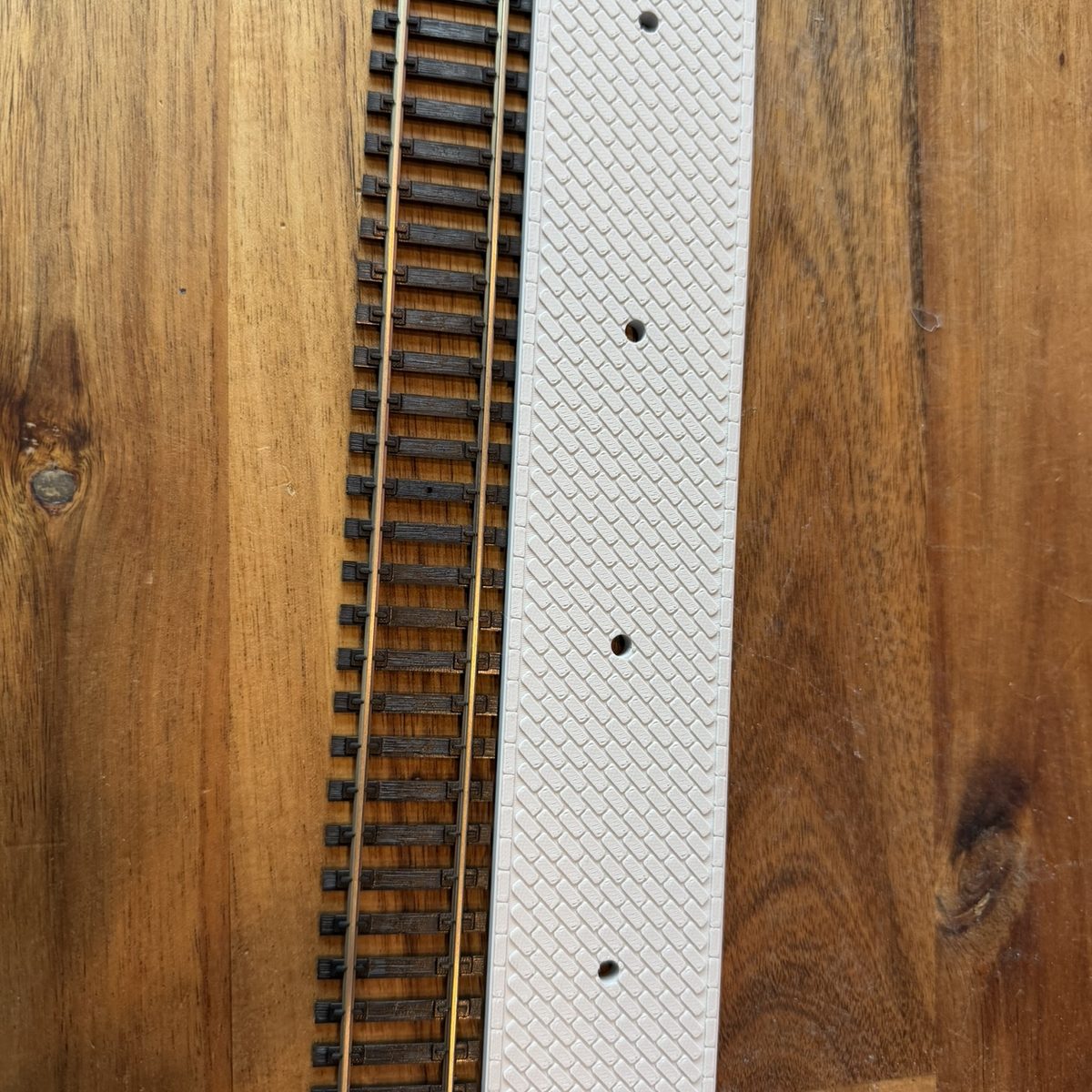 Real print: the paved 9 in platform lying beside a straight Atlas code 100 snap-track section, pillar sockets in the deck
