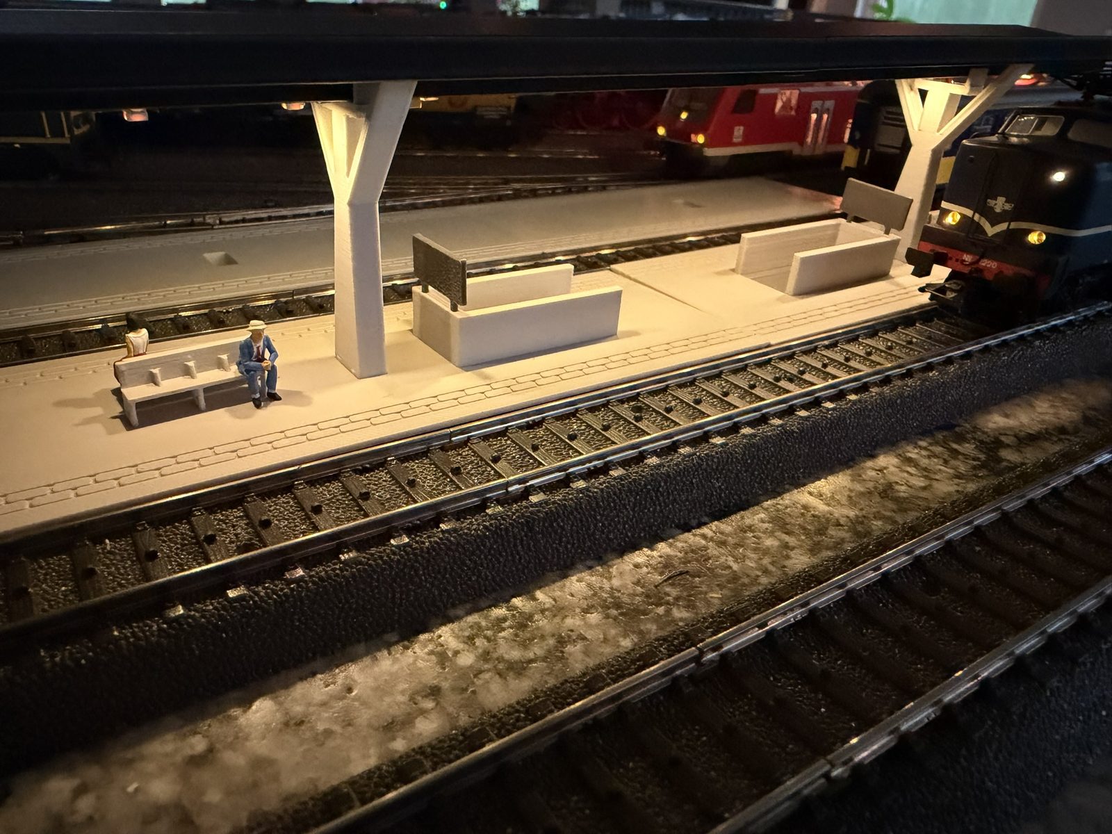 Real print: the V roof station lit at night with a locomotive drawn up alongside and passengers waiting on the bench