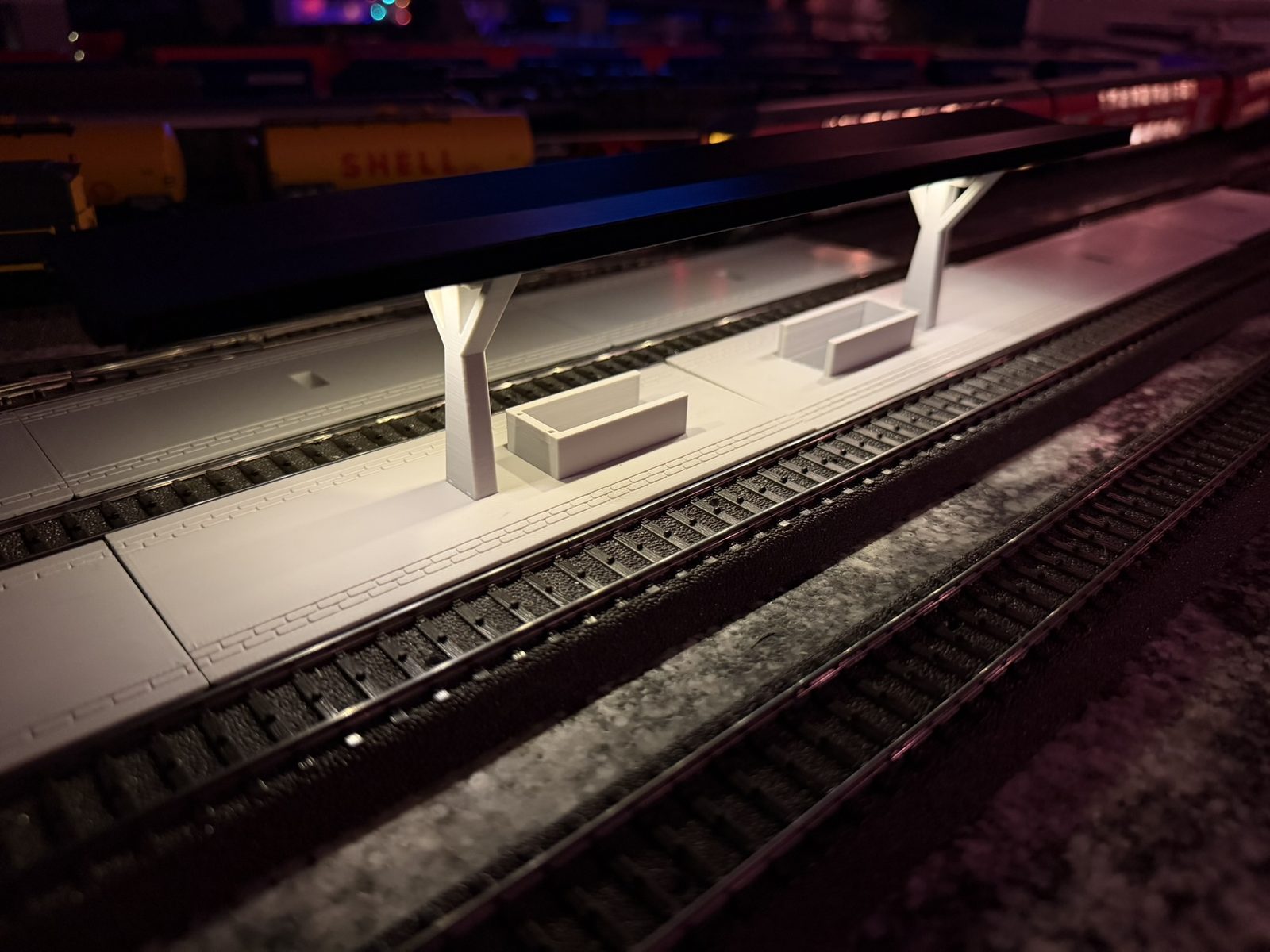 Real print: the V roof station at night on the layout, lit from the roof, trains in the background