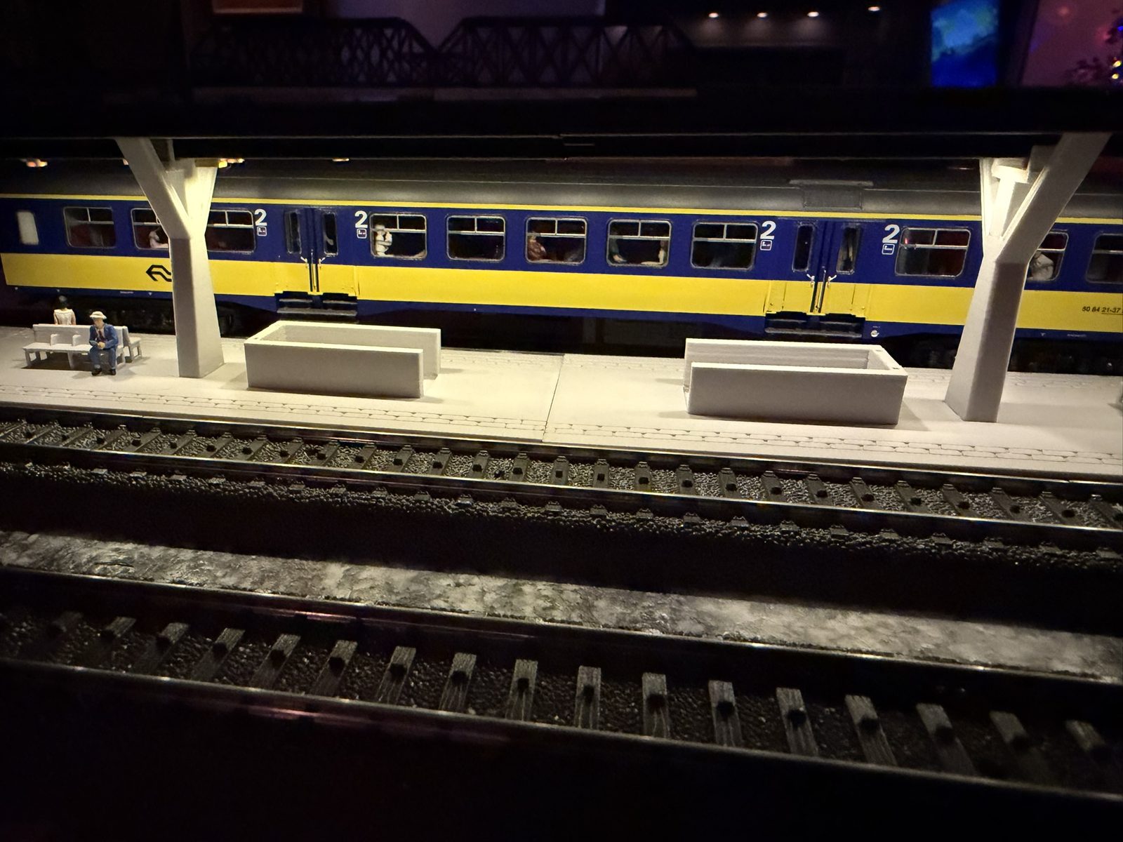 Real print: a coach stopped alongside the V roof station at night, roof light on, passengers on the bench